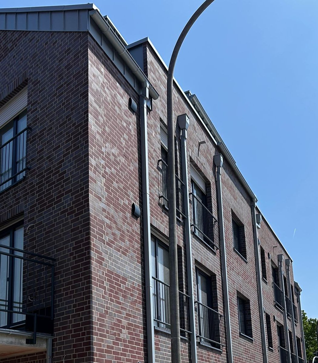 Gebäudeecke mit fertiger Klinkerfassade, Fensterlaibungen und Regenfallrohren